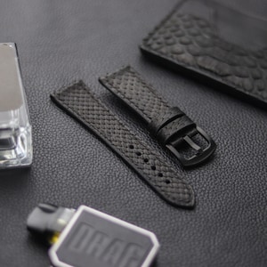 Könnte beinhalten: Zwei schwarze Uhrenarmbänder mit einem strukturierten Muster. Ein Armband hat eine schwarze Schnalle.