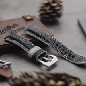 May include: Two black leather watch straps with white stitching. One strap has a silver buckle.