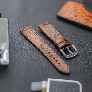 Könnte beinhalten: Zwei braune Lederarmbänder mit Schlangenhautmuster. Ein Armband hat eine silberne Schnalle.