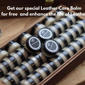 K&ouml;nnte beinhalten: Eine Holzschachtel gef&uuml;llt mit mehreren kleinen, runden Beh&auml;ltern mit Lederbalsam. Jeder Beh&auml;lter hat einen schwarzen Deckel und ein wei&szlig;es Etikett mit dem Text 'Leather Balm'. Das Bild enth&auml;lt den Text 'Get our special Leather Care Balm for free and enhance the life of Leather'.