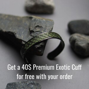 K&ouml;nnte beinhalten: Ein Armreif aus dunklem Metall mit einer strukturierten, olivgr&uuml;nen Einlage in Schuppenoptik. Der Text "Get a 40$ Premium Exotic Cuff for free with your order" ist in Wei&szlig; am unteren Bildrand aufgedruckt.