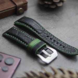 May include: Two black leather watch straps with green stitching. One strap has a green stripe down the center. Both straps have a silver buckle.