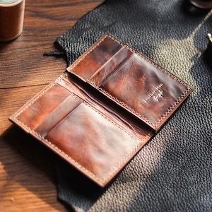 May include: Open brown leather wallet with multiple card slots and a bill compartment. The wallet has a distressed finish and visible stitching. The text "Leather Man" is embossed on the interior. The wallet is displayed open on a wooden surface.