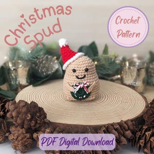 Op de afbeelding: Een gehaakte aardappel figuur, de 'Christmas Spud', met een rode en witte kerstmuts en een groene krans met een rode strik. De tekst "Christmas Spud" en "Crochet Pattern" zijn zichtbaar.