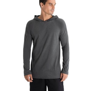 May include: A charcoal gray long-sleeve hoodie. The hoodie has a relaxed fit with a hood and long sleeves. The fabric appears to be a soft, lightweight material. The person is wearing black shorts.