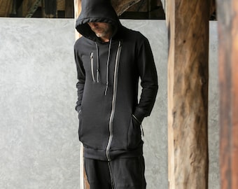Puede incluir: Sudadera con capucha negra con cremallera y silueta larga. Cuenta con una cremallera completa, dos bolsillos delanteros y un pequeño bolsillo en el pecho. La sudadera está hecha de una tela oscura y tiene una capucha con cordón.