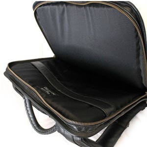 May include: Black leather briefcase with a zip closure and a top handle. The briefcase is open and the inside is lined with black fabric.