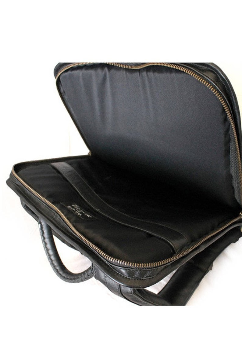May include: Black leather briefcase with a zip closure and a top handle. The briefcase is open and the inside is lined with black fabric.
