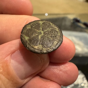 以下が含まれることがあります： 5 本の尖った星形のデザインが施された、丸いブロンズ色のボタンのクローズアップ。