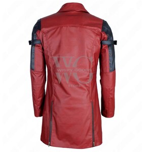 A full-length, front-facing photo of a bold, two-tone real leather trench coat/long jacket in deep red and black. The coat has a dramatic, duster-length cut and features a notched lapel collar. It contrasts red leather on the main body panels with black leather on the shoulders, inner lapels, and portions of the sleeves. The coat is highly detailed with multiple metallic accents, including functional and decorative buckles and straps on the shoulders and cuffs, gothic or rocker aesthetic.