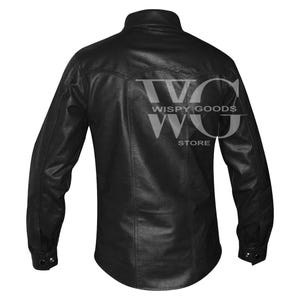 Back view of the long-sleeved black leather shirt. It highlights a curved western-style yoke across the upper shoulders with double-stitched vertical seams running down to the slightly curved hem. The cuffs on the long sleeves are finished with a single visible snap button closure. The entire garment shows a uniform pebble-grained texture.