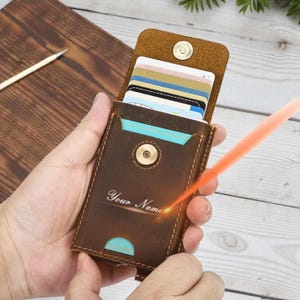 May include: A brown leather card holder with a magnetic closure, holding multiple cards. The front of the wallet is embossed with the words "Your Name". The wallet is open, revealing the cards inside.