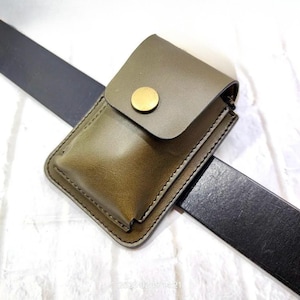 May include: Olive green leather belt pouch with a flap secured by a gold-colored button. The pouch is rectangular and stitched with a contrasting thread. A black leather belt is visible.