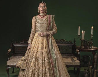 May include: A long, flowing, golden-yellow gown with intricate embroidery and a matching purse. The dress features long sleeves and a full skirt, complemented by a sheer, patterned shawl with red and green accents. The ensemble is accessorized with jewelry.