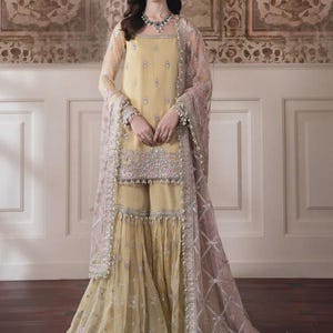 May include: A light yellow embroidered ensemble featuring a long-sleeved tunic, wide-leg pants, and a sheer, patterned shawl. The outfit is adorned with intricate silver embroidery and delicate embellishments, creating an elegant and formal look.