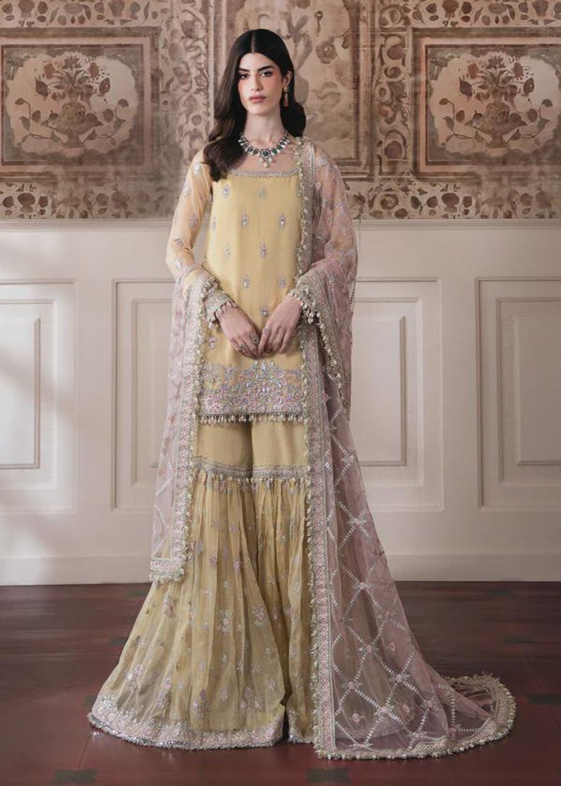 May include: A light yellow embroidered ensemble featuring a long-sleeved tunic, wide-leg pants, and a sheer, patterned shawl. The outfit is adorned with intricate silver embroidery and delicate embellishments, creating an elegant and formal look.