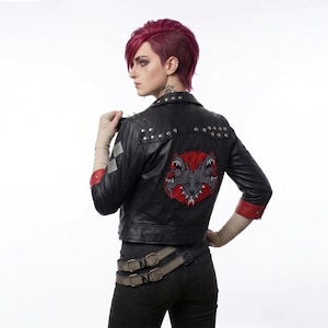 May include: Black leather jacket with silver studs and a red and grey monster patch on the back. The jacket has a classic biker style with a notched collar and a zip-up front. The sleeves have red accents and is worn with black trousers.