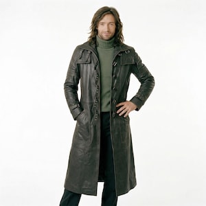 Puede incluir: Un abrigo largo de cuero marrón oscuro con cierre de botones y bolsillos. El abrigo llega hasta los tobillos. La persona lleva un jersey de cuello alto verde y pantalones negros. La longitud del abrigo es de unos 152 cm.