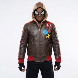 May include: A brown leather jacket with a tan hood, red ribbed cuffs, and a front zipper. The chest features a red Spider-Man emblem, a blue circular patch, and a yellow silhouette figure. The sleeves have red stripes and black fingerless gloves.