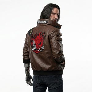 May include: Brown leather jacket with a red and white graphic on the back. The jacket has a black collar with the word "SAMURAI" and multiple pockets. The sleeves have a black cuff. The person is wearing dark blue jeans.
