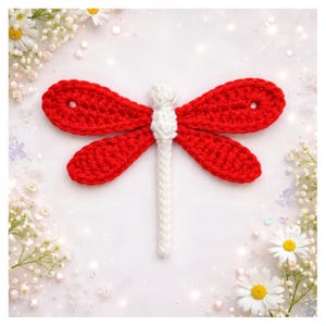 May include: A handmade crochet dragonfly with red wings and a white body. The dragonfly is surrounded by white flowers and greenery on a white background. The wings have small holes.