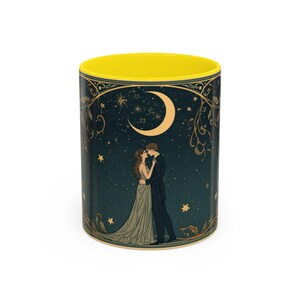 Puede incluir: Una taza de café de cerámica con interior amarillo y una ilustración romántica. El diseño presenta una pareja abrazándose bajo una luna creciente y estrellas sobre un fondo azul oscuro. Elementos florales decorativos dorados enmarcan la escena.