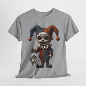 Puede incluir: Camiseta gris con un diseño de payaso aterrador. El payaso tiene una cara blanca, ojos negros y un gorro de bufón rojo y azul. El payaso viste un atuendo rojo y azul y sostiene un objeto rasgado.