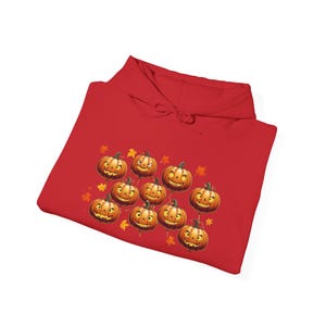 Puede incluir: Una sudadera con capucha roja con un diseño de Halloween. El diseño incluye varias calabazas sonrientes y hojas de otoño. La sudadera está hecha de un material suave, ideal para el otoño.