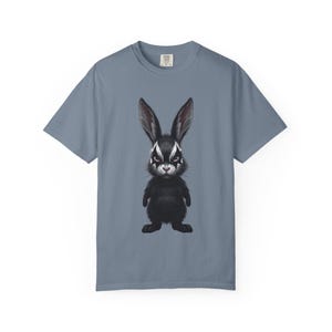 Puede incluir: Una camiseta azul grisáceo con una ilustración detallada de un conejo negro con marcas blancas en la cara. El conejo tiene orejas largas y está de pie. La camiseta está hecha de un material suave.