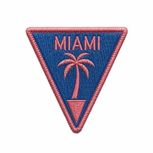 May include: A triangular embroidered patch featuring a blue background with a pink border. The word MIAMI is stitched in pink letters above a pink palm tree graphic that sits inside a small pink triangle at the bottom of the patch.