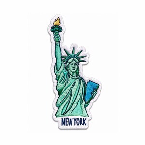 Puede incluir: Un parche bordado que representa la Estatua de la Libertad en tonos verde azulado y verde, sosteniendo una antorcha amarilla y una tableta azul. La base del parche incluye el texto NEW YORK en letras mayúsculas azul oscuro sobre fondo blanco.