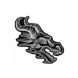 Könnte beinhalten: Ein bestickter Aufnäher mit schwarzem Hintergrund und einem in Weiß gestickten Drachenschädel-Motiv. Der Drachenschädel ist im Profil dargestellt und zeigt detaillierte Hörner, scharfe Zähne und einen gezackten Kiefer in weißem Garn.
