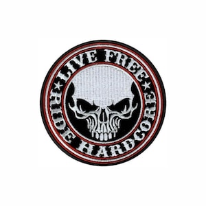 May include: A circular embroidered patch featuring a white skull centered on a black background. The border contains the white text "LIVE FREE" and "RIDE HARDCORE" separated by two small stars, all enclosed within a thin red and black ring.