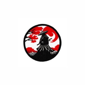 May include: A circular embroidered patch featuring a black silhouette of a figure wearing a conical hat and holding a sword. The background displays a vibrant red sun, white sky, and black tree branches, all enclosed within a thick black border.