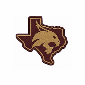 Könnte beinhalten: Ein kastanienbrauner, bestickter Aufnäher in Form des Bundesstaates Texas mit einer goldenen Silhouette eines Rotluchskopfes. Der Aufnäher hat einen dicken goldenen Rand, der die Staatsform und das Luchsmotiv umreißt und einen Kontrast erzeugt.