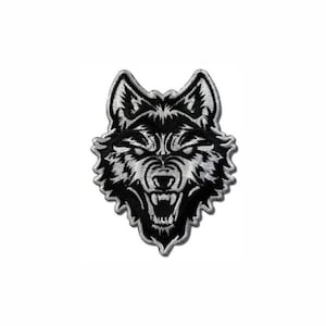 Puede incluir: Un parche bordado que muestra la cabeza de un lobo gruñendo. El diseño está realizado con hilo blanco y negro de alto contraste, destacando texturas de pelaje detalladas, orejas puntiagudas y una boca abierta con dientes visibles en expresión feroz.