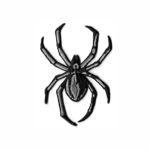 Peut inclure: Un écusson brodé en forme d'araignée. Le motif présente un corps et des pattes noirs avec des détails en fil gris argenté sur l'abdomen et le long de chacune des huit pattes, créant un aspect texturé avec un contraste élevé.
