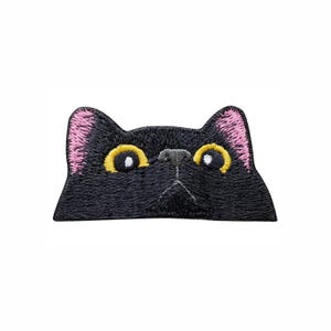 May include: An embroidered patch featuring the head of a black cat with pointed ears, pink inner ear details, bright yellow eyes with black pupils, and a small grey nose, designed to look like a cat peeking over a straight horizontal edge.