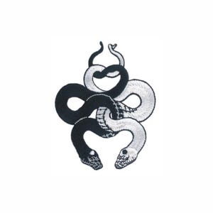 May include: An embroidered patch featuring two intertwined snakes, one solid black and one solid white, forming a symmetrical knot design. The snakes have detailed scale patterns on their heads and bodies, creating a high-contrast graphic emblem.