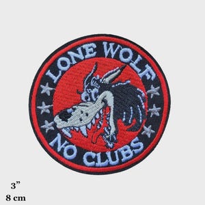May include: Embroidered patch with a cartoon wolf design. The patch is circular, with a red center and black border. Text reads "LONE WOLF" and "NO CLUBS". The patch measures 3 inches (7.6 cm) in diameter.