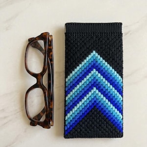 Könnte beinhalten: Eine Brille mit Schildpatt-Fassung neben einem schwarzen Brillenetui mit blauem Zickzackmuster. Das Etui besteht aus einem gewebten Material mit Blau- und Weißtönen.