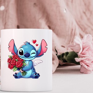 May include: White ceramic mug featuring a cartoon illustration of a blue alien character holding a bouquet of red roses. The character has large ears, a winking eye, and small angel wings. Two red hearts float above the character.