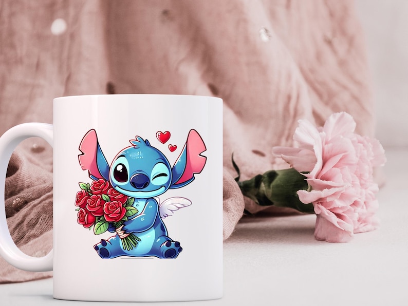 May include: White ceramic mug featuring a cartoon illustration of a blue alien character holding a bouquet of red roses. The character has large ears, a winking eye, and small angel wings. Two red hearts float above the character.