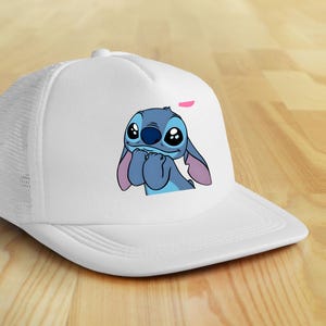 May include: White trucker hat featuring a cartoon image of Stitch from Lilo & Stitch. The character is blue with large eyes and pink ears. The hat has a mesh back and a curved brim.
