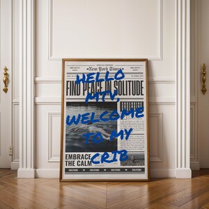 Peut inclure: Une impression encadrée d'un journal avec le texte "New York Times" et les mots "HELLO, FIND PEACE IN SOLITUDE, MTV, WELCOME TO MY CRIB, EMBRACE THE CALM" écrits en peinture bleue.