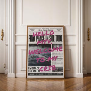May include: A framed print with a newspaper-style design featuring the text "New York Times" and the words "Find peace in solitude, welcome to my crib" written in pink.