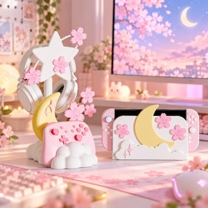 Könnte beinhalten: Ein weiß-rosa Gaming-Zubehörset bestehend aus einem Kopfhörerständer mit Stern und Kirschblüten, einer Controller-Ladestation mit gelbem Halbmond und Wolken sowie einer Konsolen-Dockingstation mit gelbem Mond, Wolken und rosa Kirschblüten.
