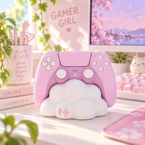 Pode incluir: Um comando de jogo sem fios cor-de-rosa pastel pousado numa base de carregamento branca em forma de nuvem. A base apresenta dois pequenos &iacute;cones de estrelas cor-de-rosa na parte frontal. O comando tem joysticks, D-pad e bot&otilde;es brancos.