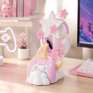 Puede incluir: Un soporte para accesorios de juego blanco y rosa con un soporte para auriculares en forma de estrella adornado con flores de cerezo rosas, un acento de luna creciente y una base en forma de nube para sostener un mando de juego inalámbrico.