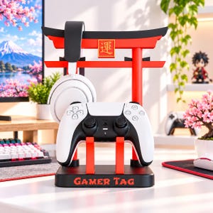 Peut inclure: Un support pour accessoires de jeu noir et rouge en forme de porte torii, avec une manette sans fil blanche et un casque noir et blanc. La base affiche le texte GAMER TAG en orange et une petite plaque carrée avec le kanji 運.
